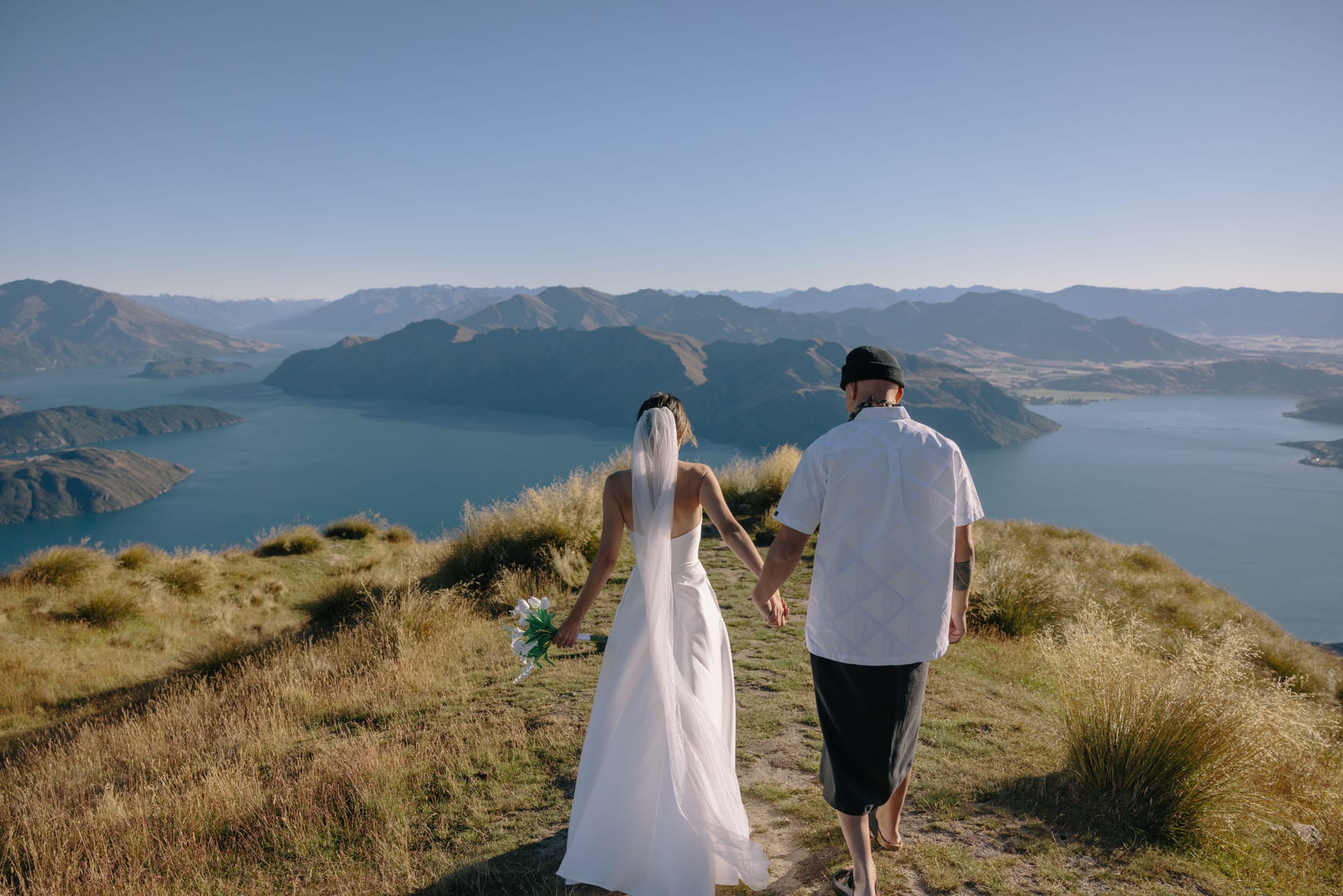 A couple walking the ridge, the groom in shorts, the bride’s veil lifting