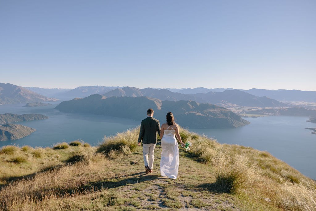 A couple walking a tussock ridge high above a lake, the Southern Alps beyond them